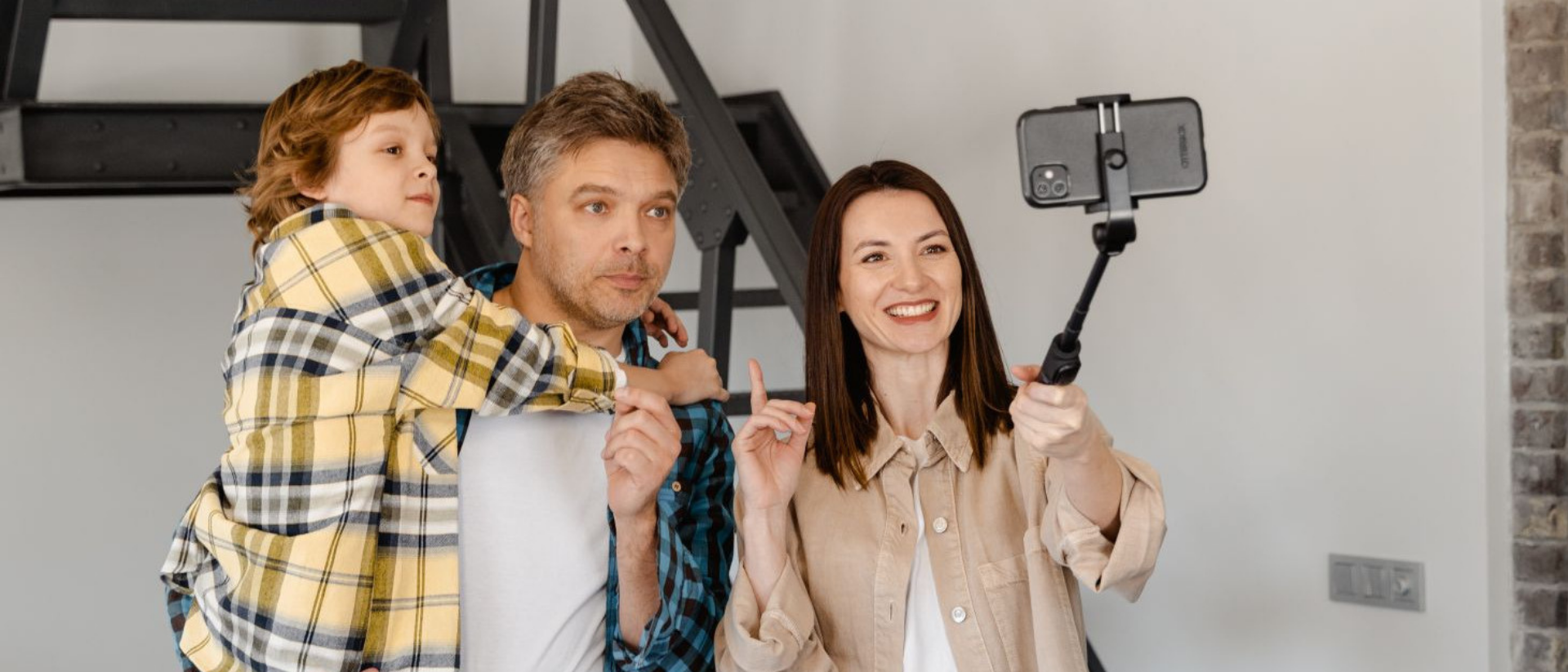 Mutter macht mit Selfiestick ein Foto von ihrer Familie mit Kind