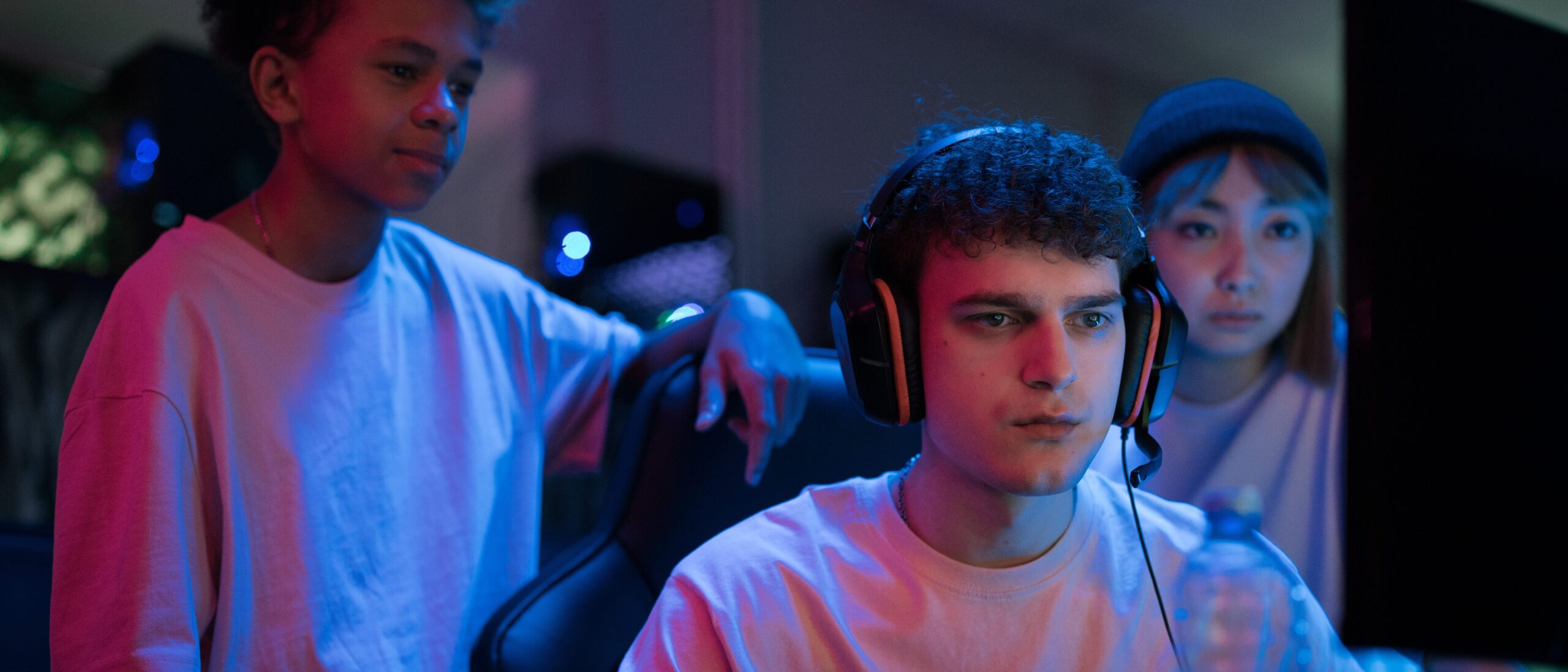 Gamer sitzt vor seinem PC mit der Konsole in der Hand, hinter ihm stehen Zuschauer