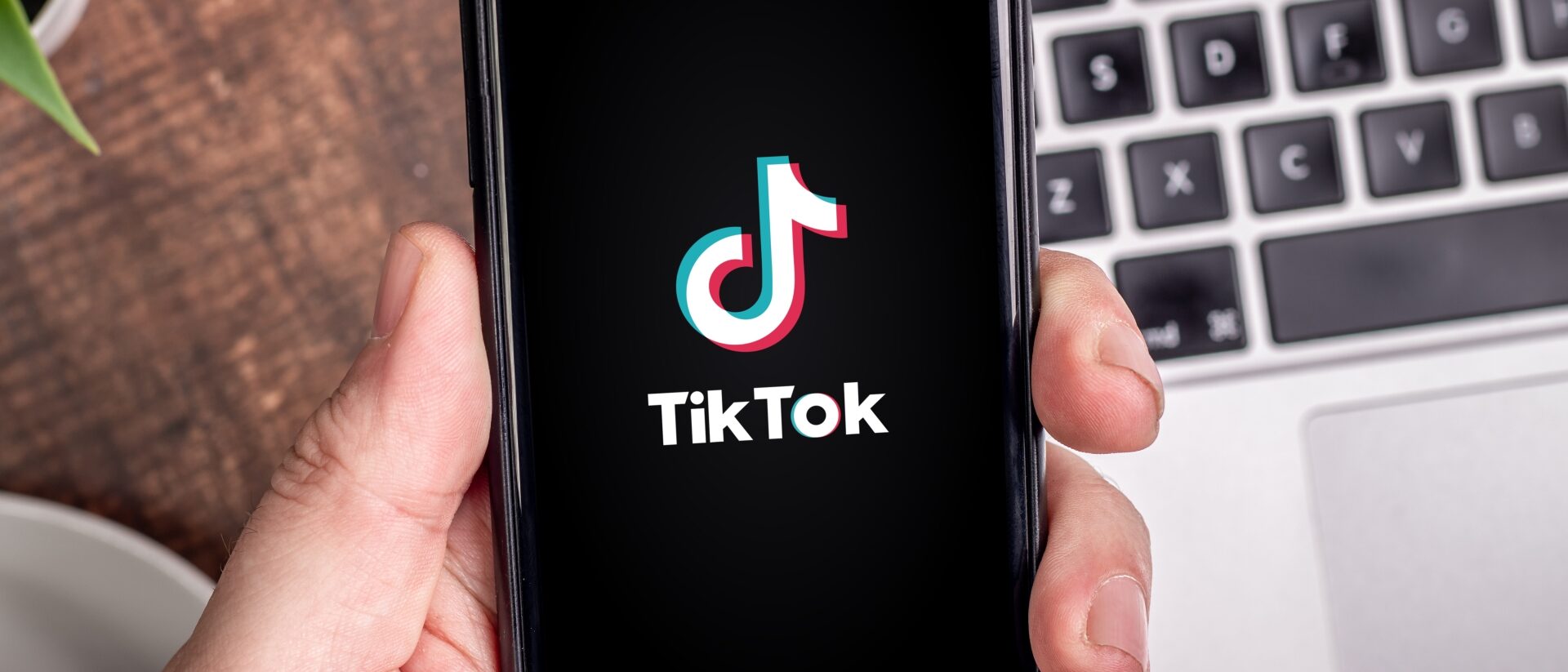 Hand hält Handy auf der das TikTok Startbild angezeigt wird
