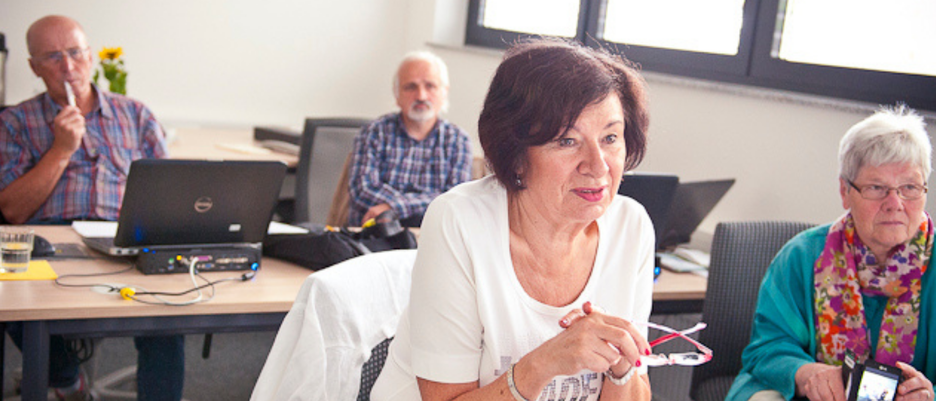 Merhere ältere Menschen sitzen an Tischen in einem Seminar
