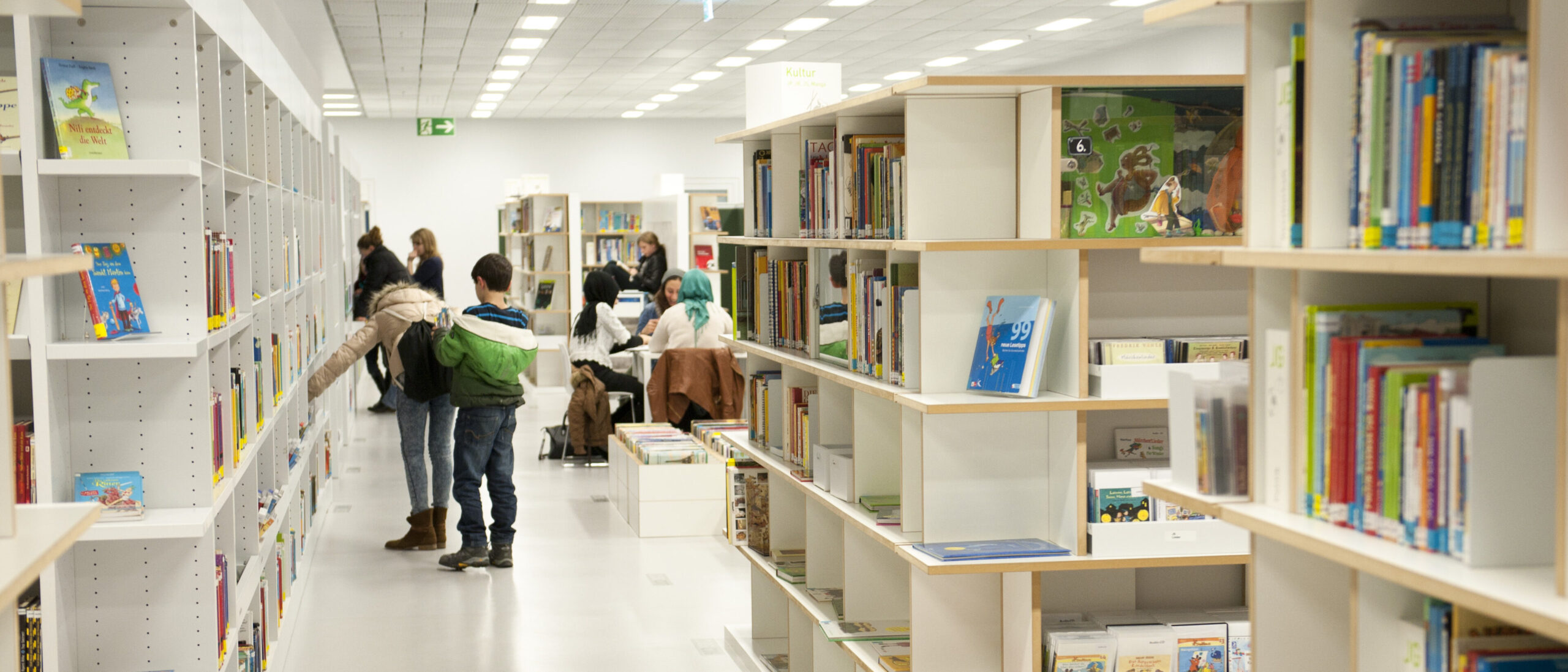 Bibliotheksregale aus denen sich Menschen Bücher nehmen.