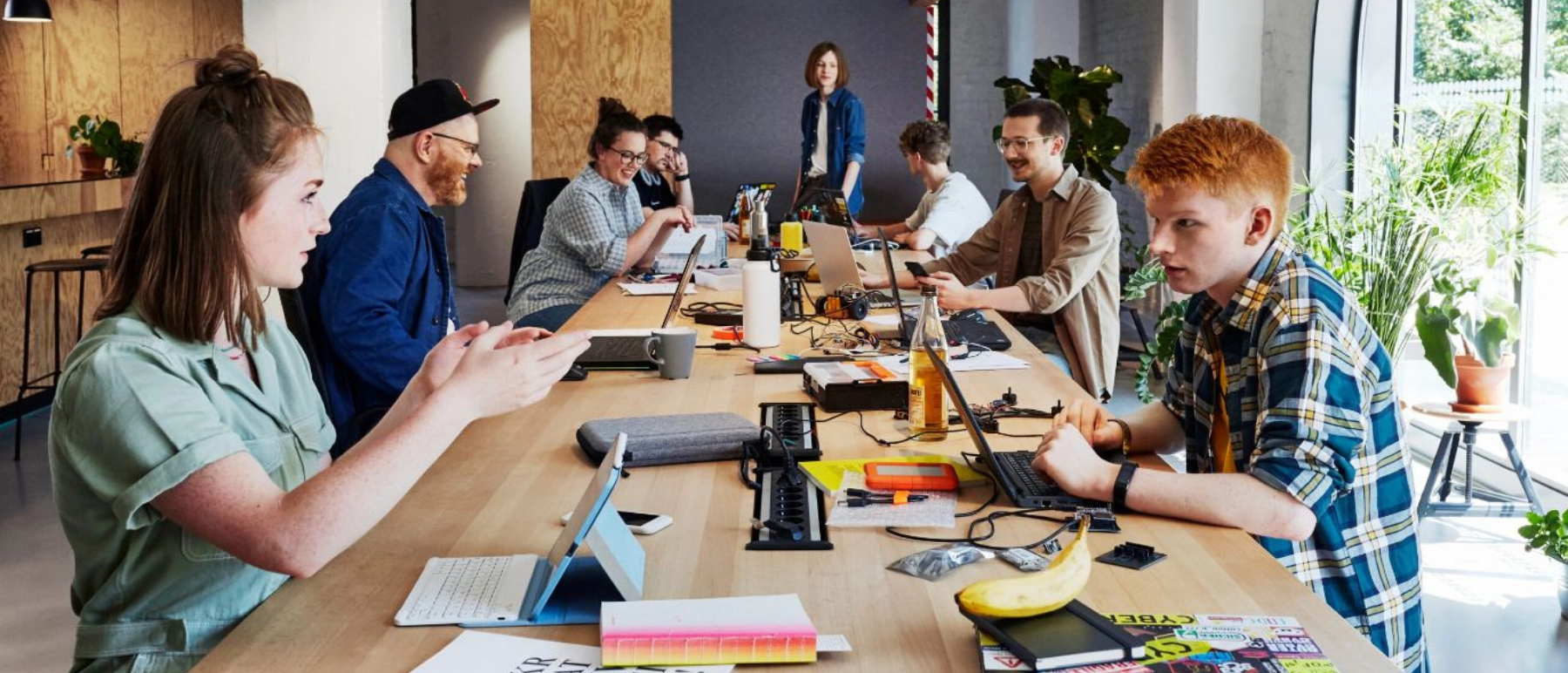 Mehrer Menschen sitzen sich an einem langen Tisch mit ihren Laptops gegenüber