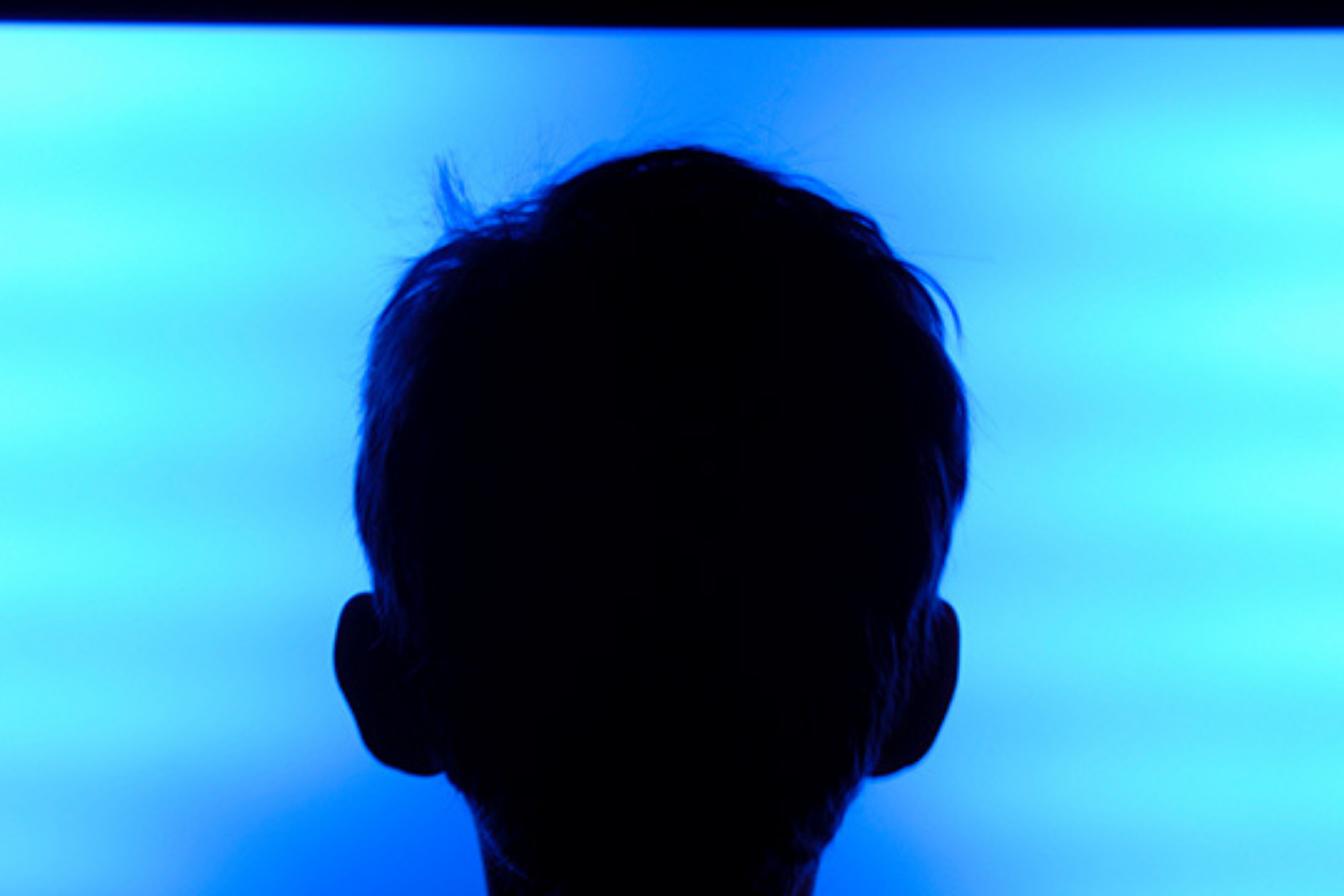 Dunkler Hinterkopf eines Jungen, der vor einem großen Screen sitzt.