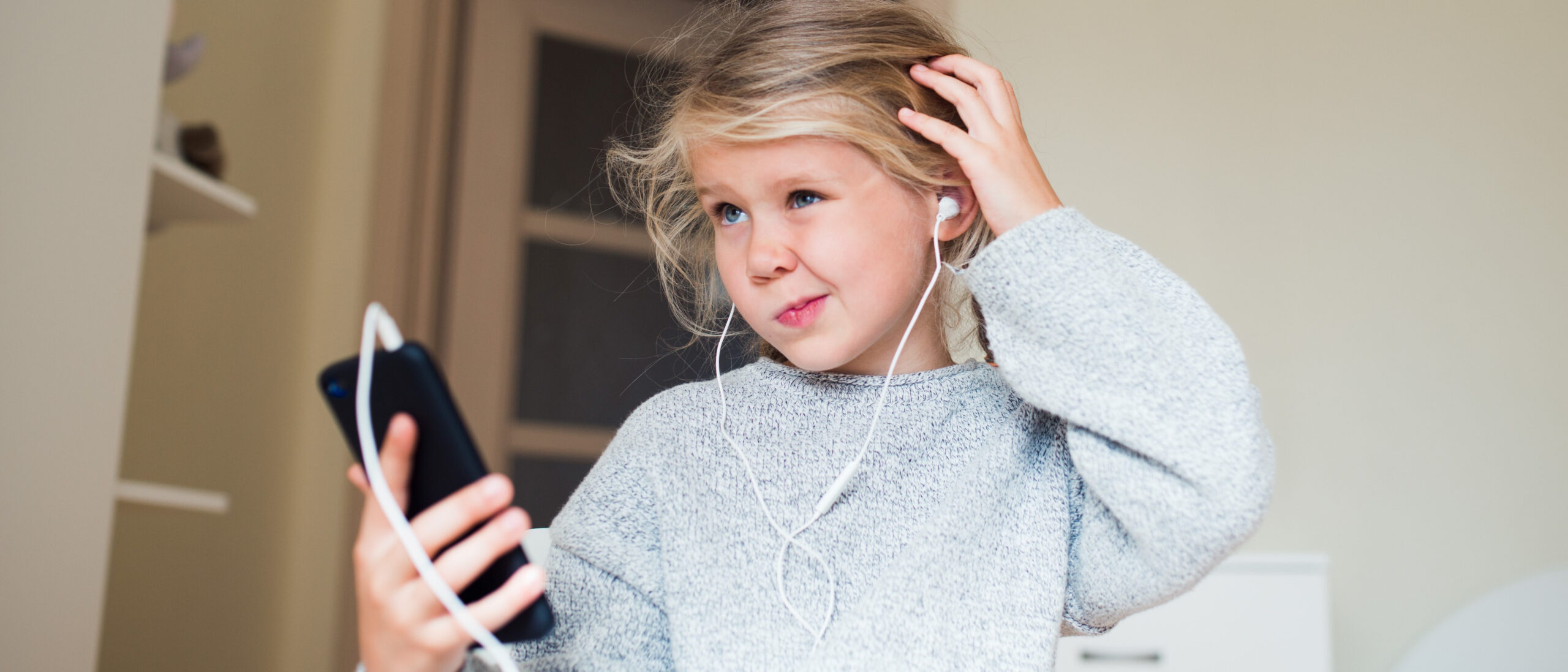 Mädchen mit Handy in der Hand krazt sich fragend am Kopf