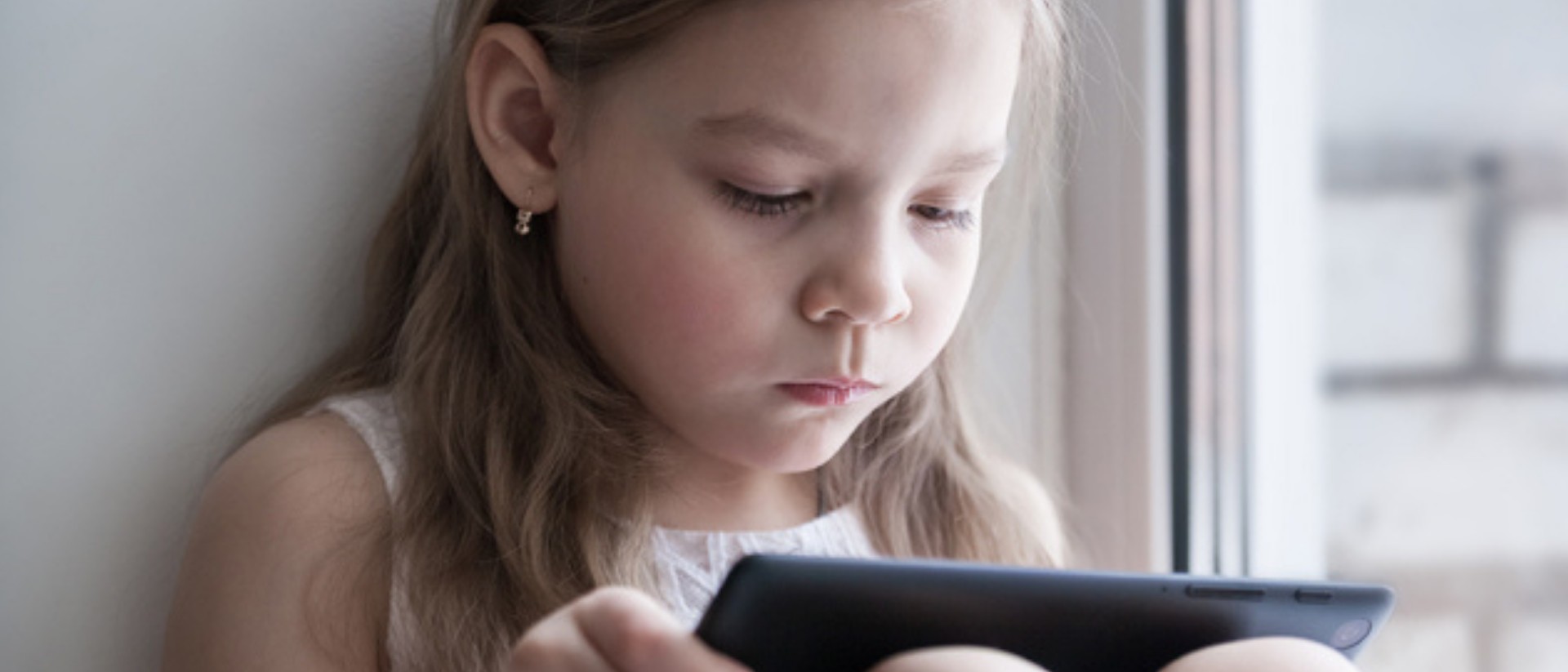 Kind sitzt auf dem Boden und und schaut in ein Tablet