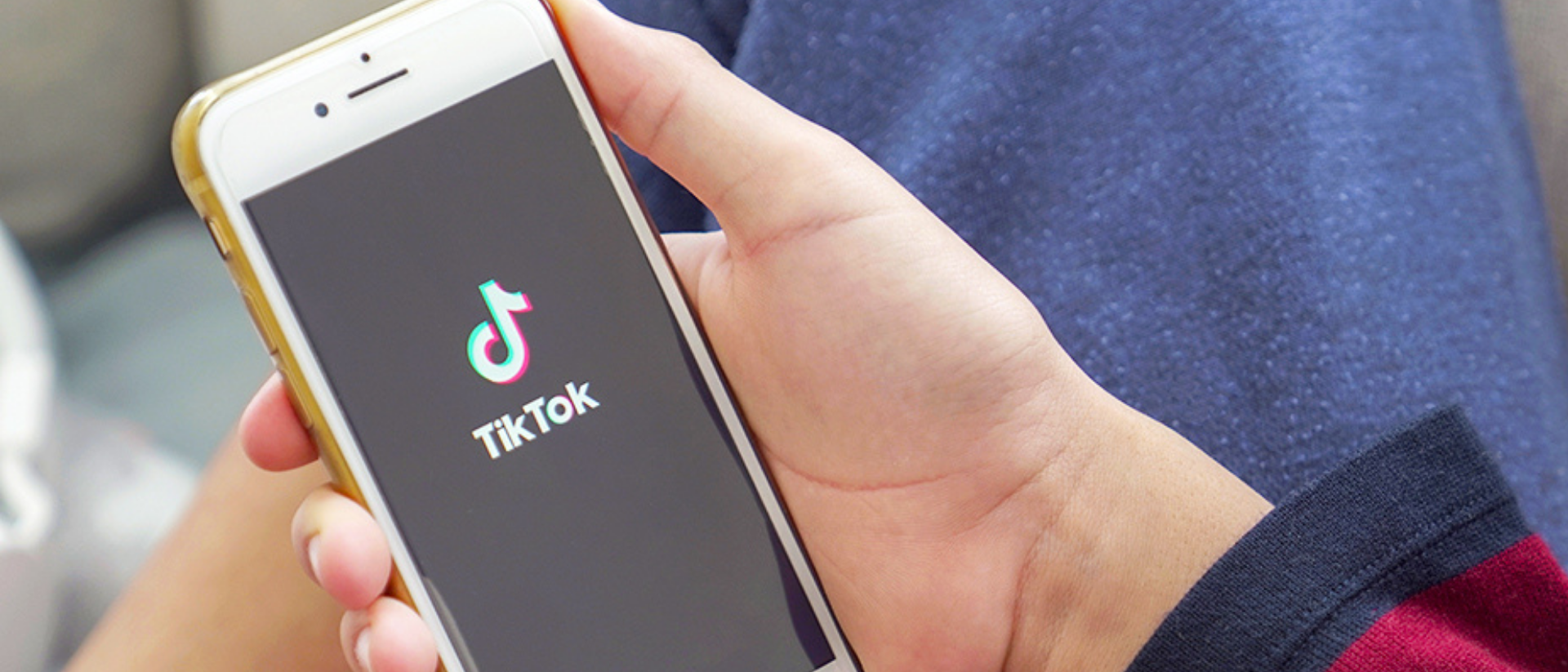Hand hält ein Handy auf derm der TikTok Startscreen angezeigt wird