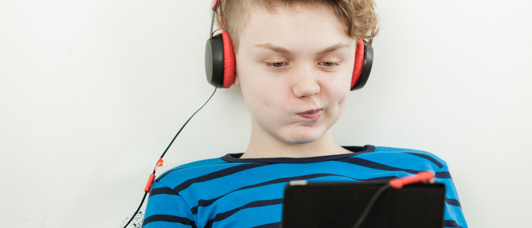 Junge sitzt mit Köpfhörern vor einem Tablet und schaut kritisch