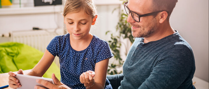 Ein Mädchen sitzt mit ihrem Vater vor dem Tablet