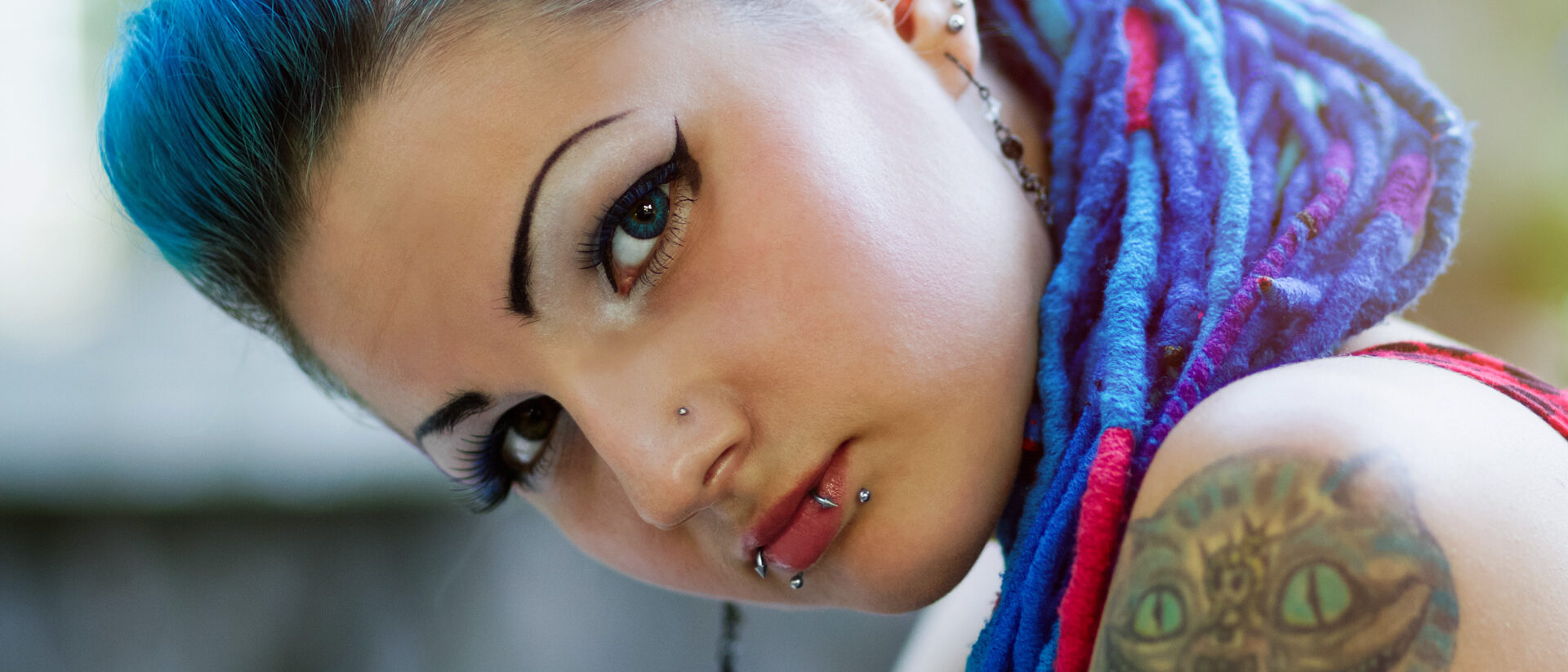 Tätowierte, gepiercte, stark geschminkte Frau mit blauen Haaren, schaut eindringlich in die Kamera