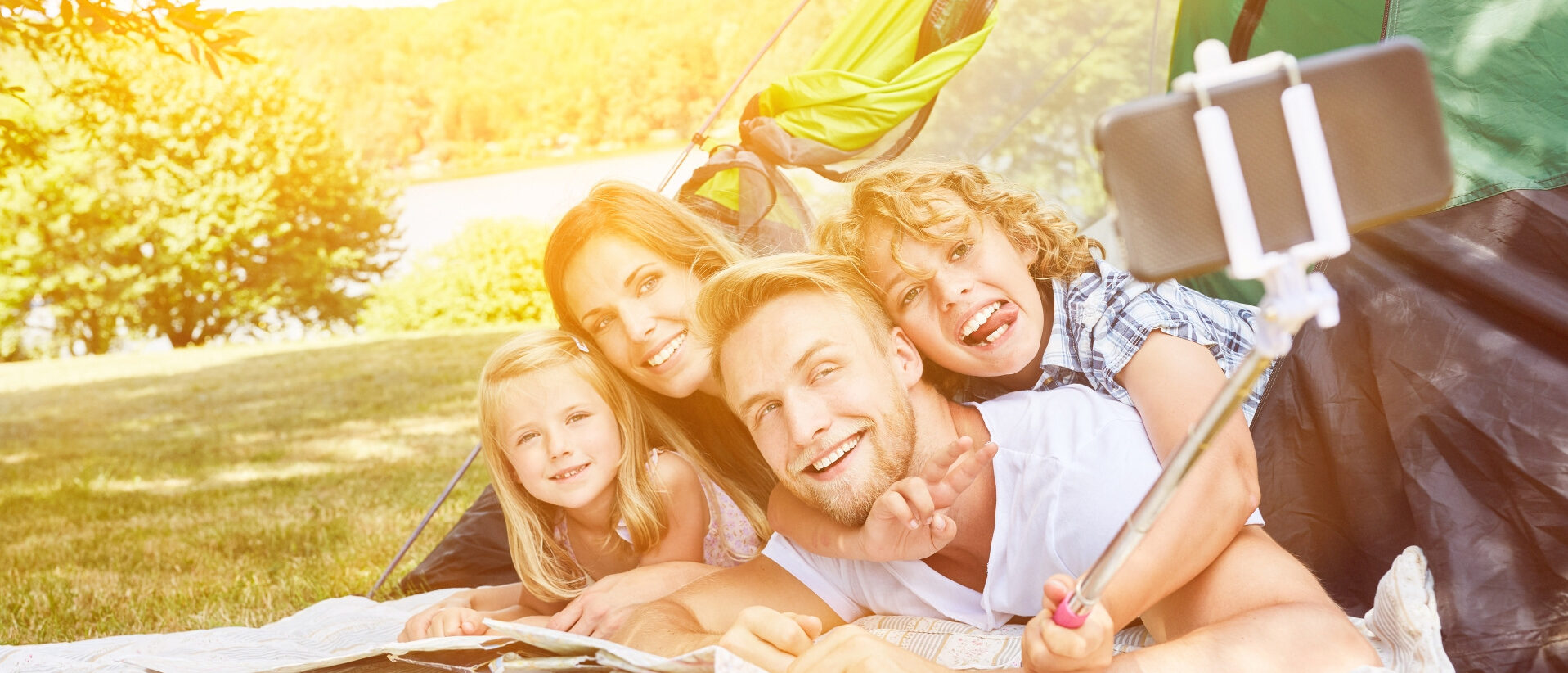 Eltern mit zwei Kinder liegen vor ihrem Zelt und machen ein Selfie.