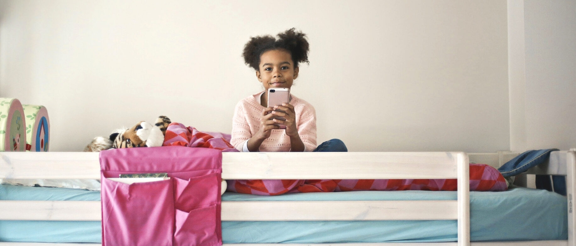 Kleines Mädchen sitzt auf ihrem Bett und hält ein Smartphone in den Händen