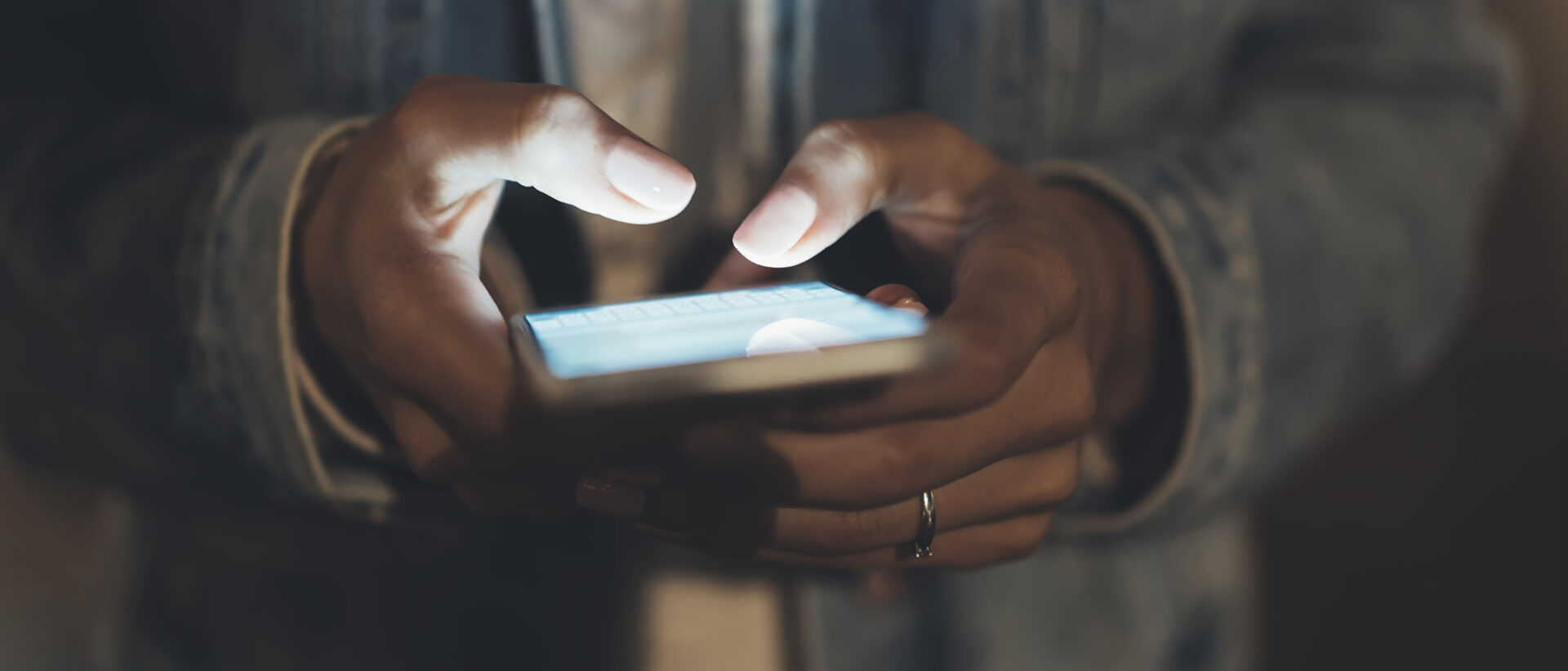 Zwei Hande die ein Smartphone halten, dessen Bildschirm hell erleuchtet ist