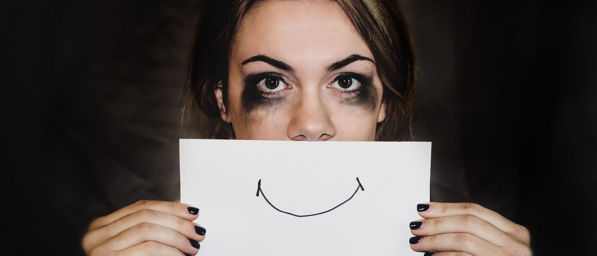 Ein Mädchen mit von Tränen verschwommener Schminke hält sich ein Blatt Papier mit einem lächelnden Mund unter die Nase