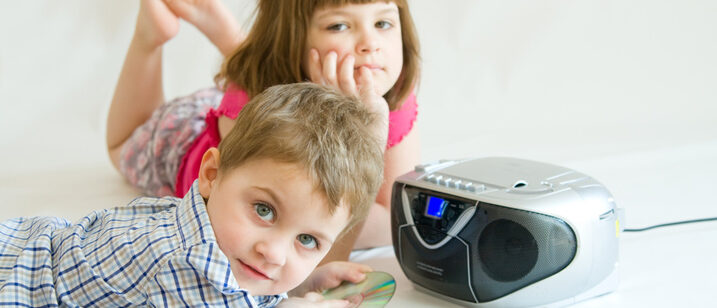 Zwei Kinder liegen vor einem Lautsprecher und hören zu.