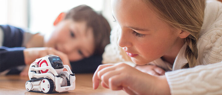 Zwei Kinder schauen fasziniert auf einen kleinen, fahrenden Roboter.