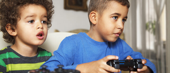 Zwei kleine Jungs schauen gebannt auf einen Bildschirm, einer hält eine Spielekonsole in der Hand.
