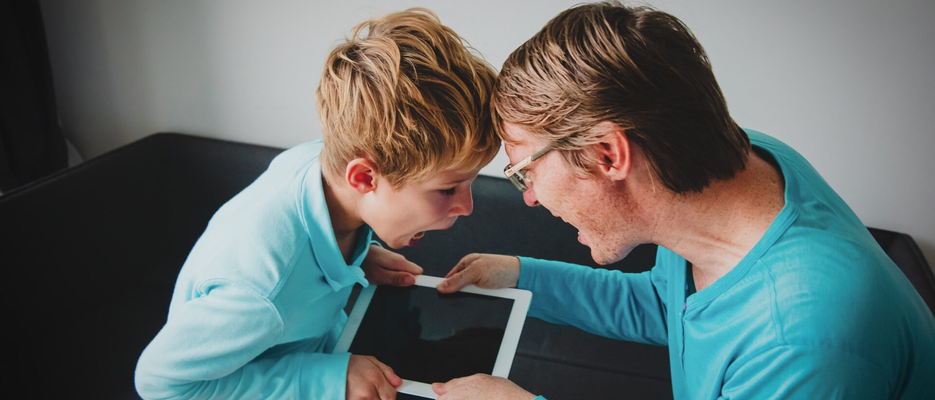 Vater und Sohn zerren an einem Tablet, um das sie sich streiten