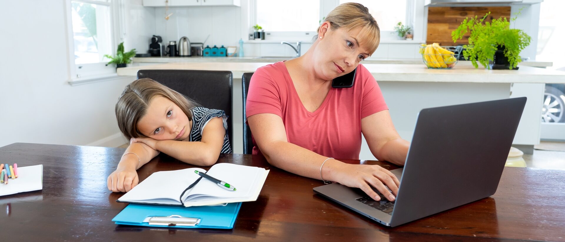 telefonierende Mutter am Laptop während Kind mit Hausaufgaben genervt daneben sitzt