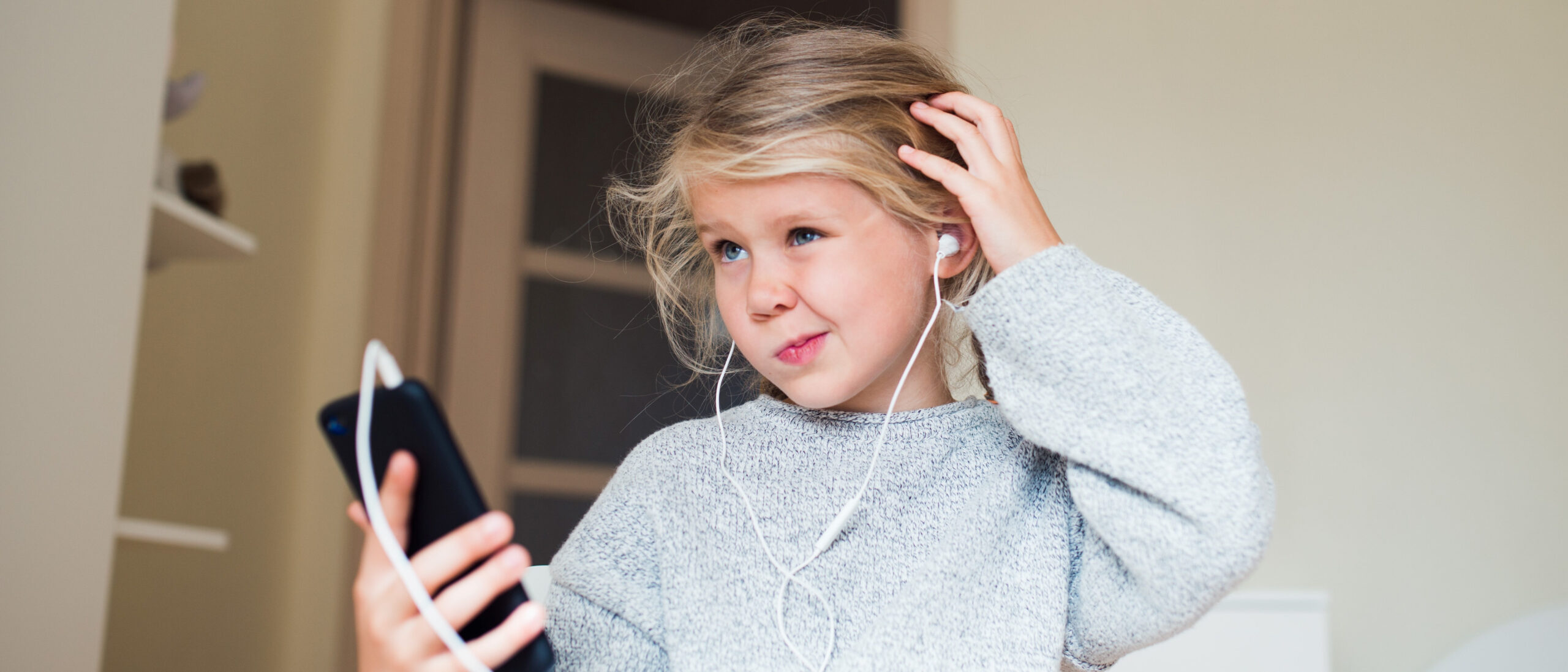 Mädchen mit Handy in der Hand krazt sich fragend am Kopf
