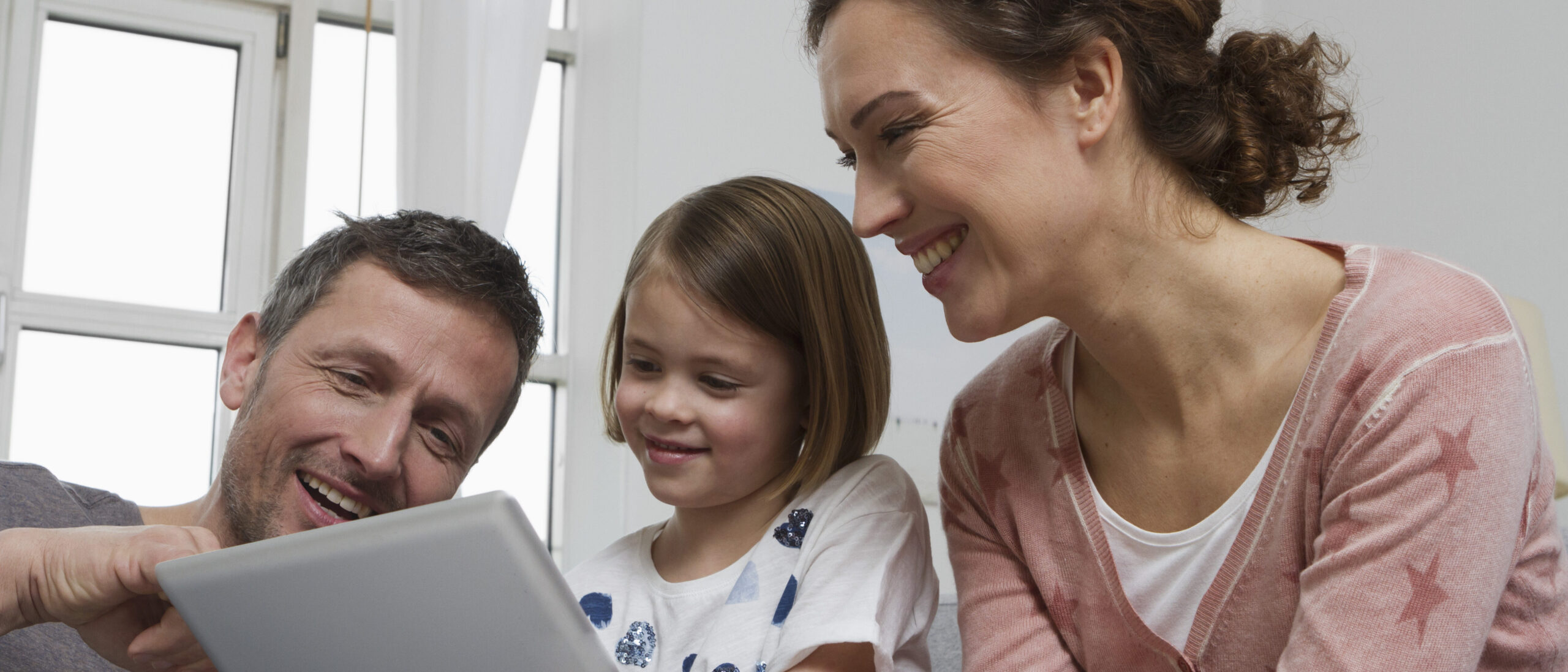 Eltern schauen gemeinsam mit ihrm Kind ins iPad