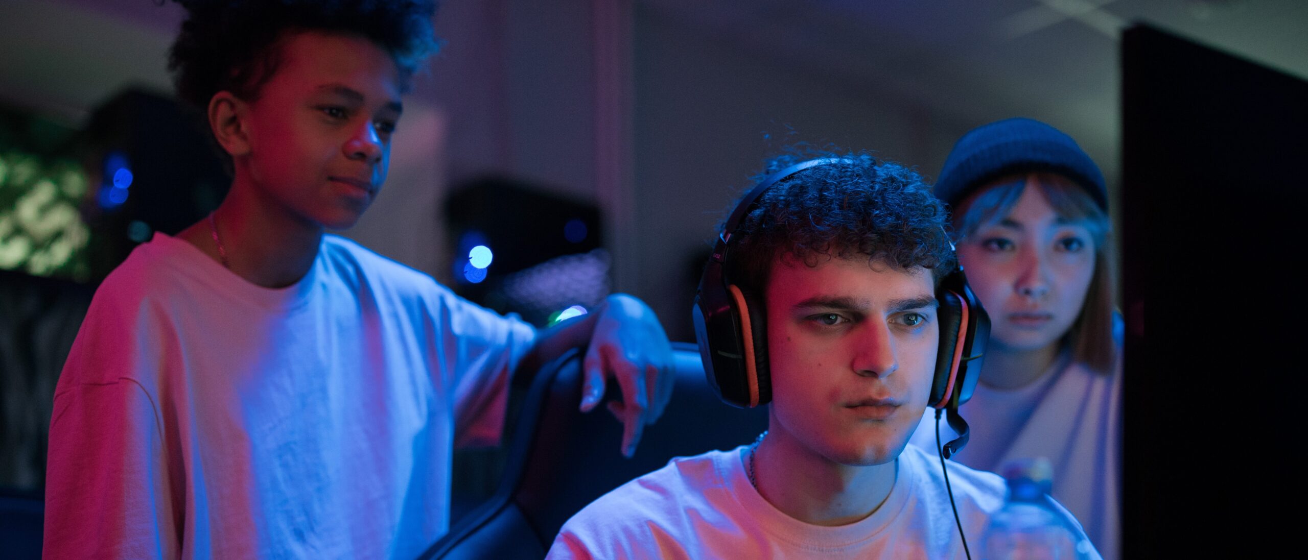 Gamer sitzt vor seinem PC mit der Konsole in der Hand, hinter ihm stehen Zuschauer