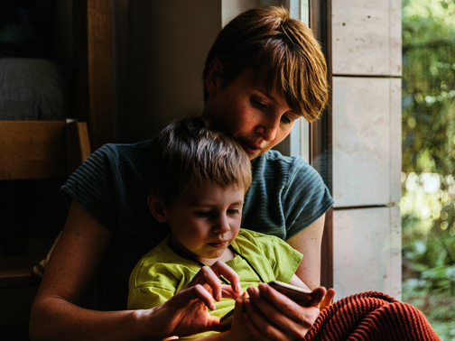 Ein Kind sitzt auf dem Schoß seiner Mutter. gemeinsam schauen sie in ein Handy