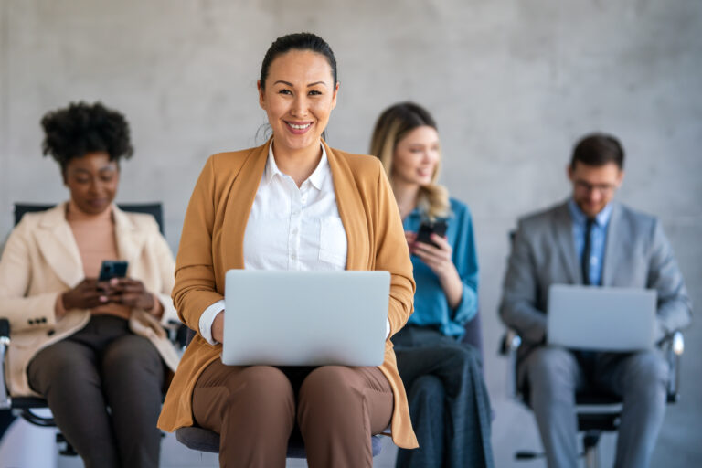 Auf verteilten Stühlen sitzen Menschen und arbeiten an Handys oder Laptops.