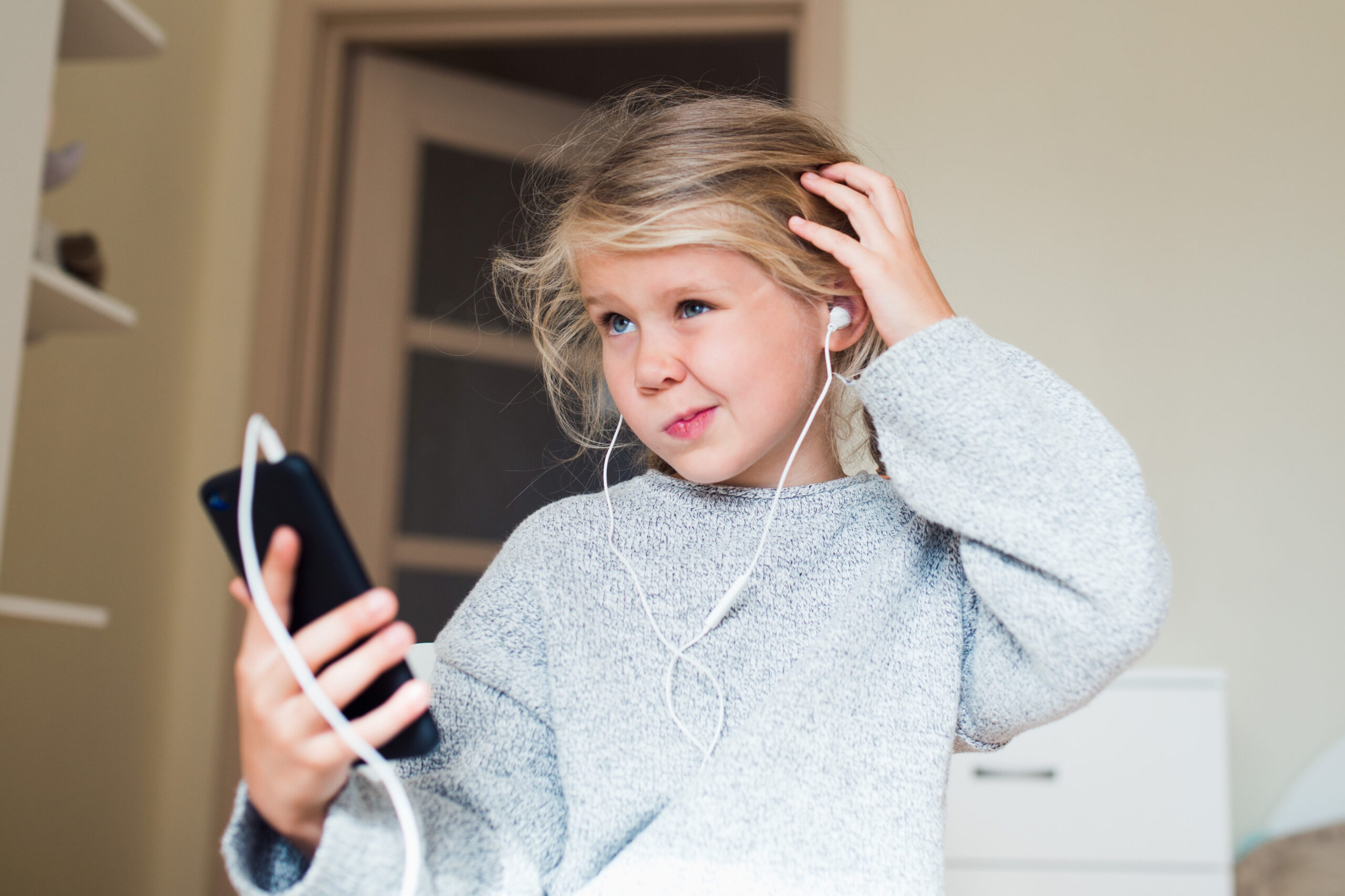 Mädchen mit Handy in der Hand krazt sich fragend am Kopf