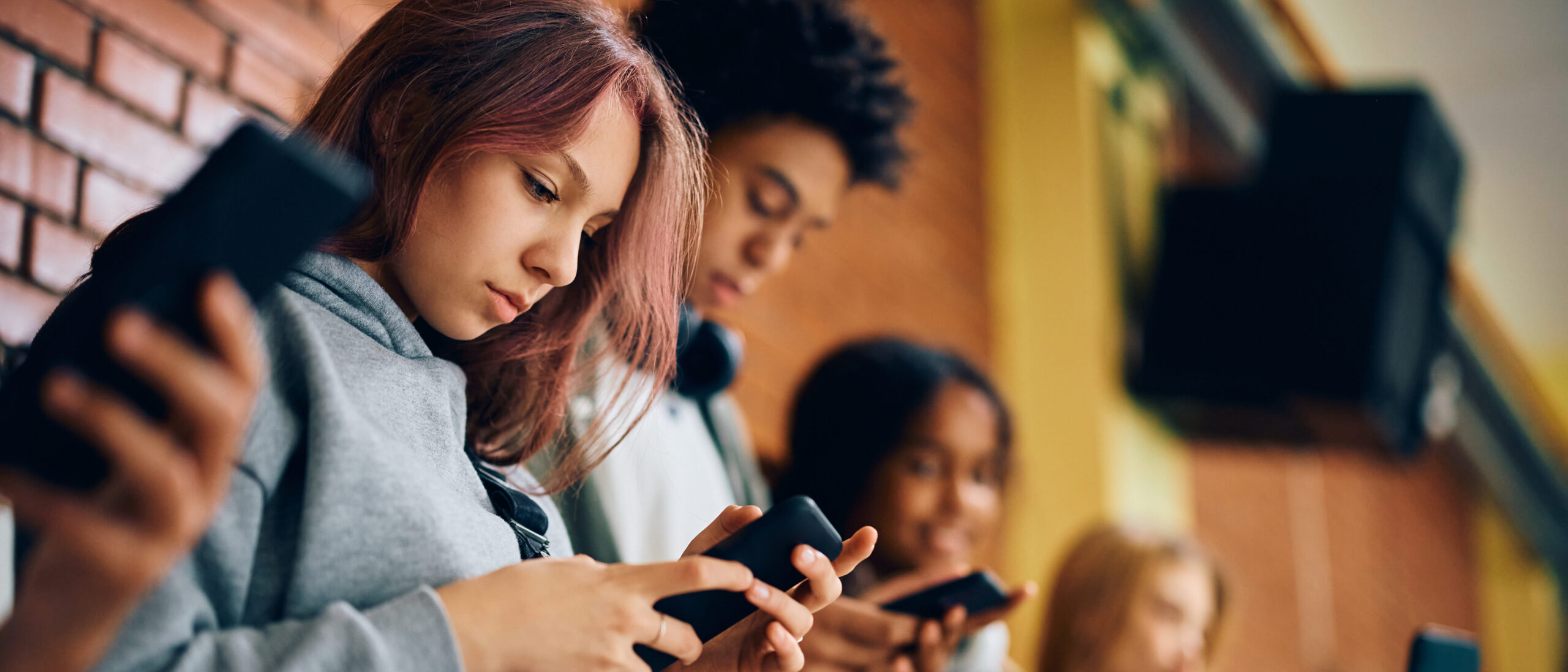 Gruppe von Teenagern, die Mobiltelefone im Flur der Schule benutzen.