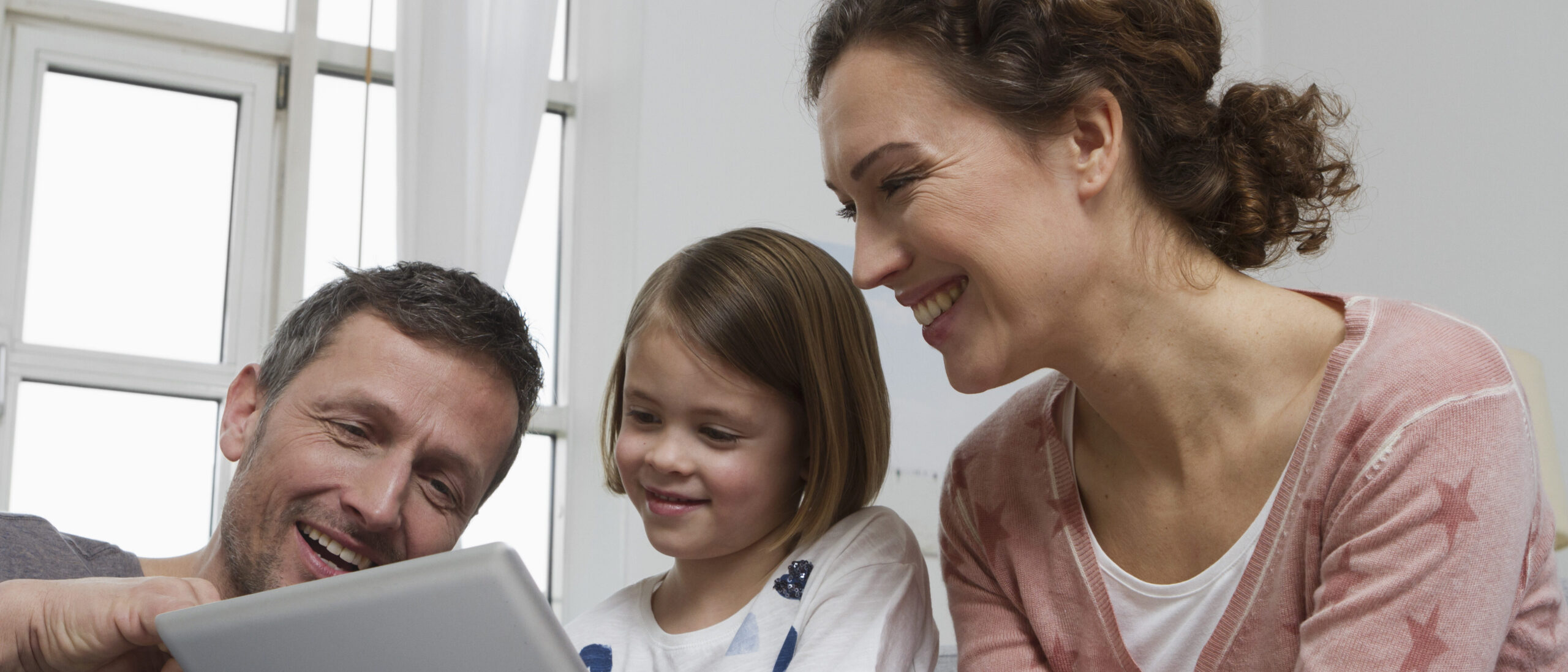 Eltern schauen gemeinsam mit ihrm Kind ins iPad