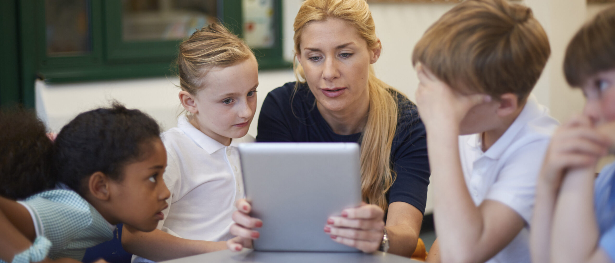 Der Lehrer zeigt den Schülern Inhalte auf einem Tablet in einem hell beleuchteten Klassenzimmer.