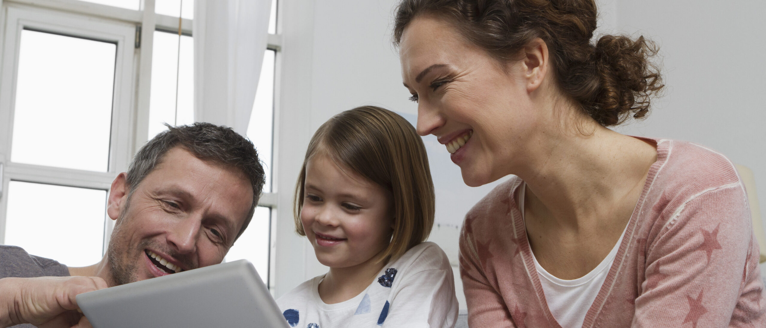 Eltern schauen gemeinsam mit ihrm Kind ins iPad