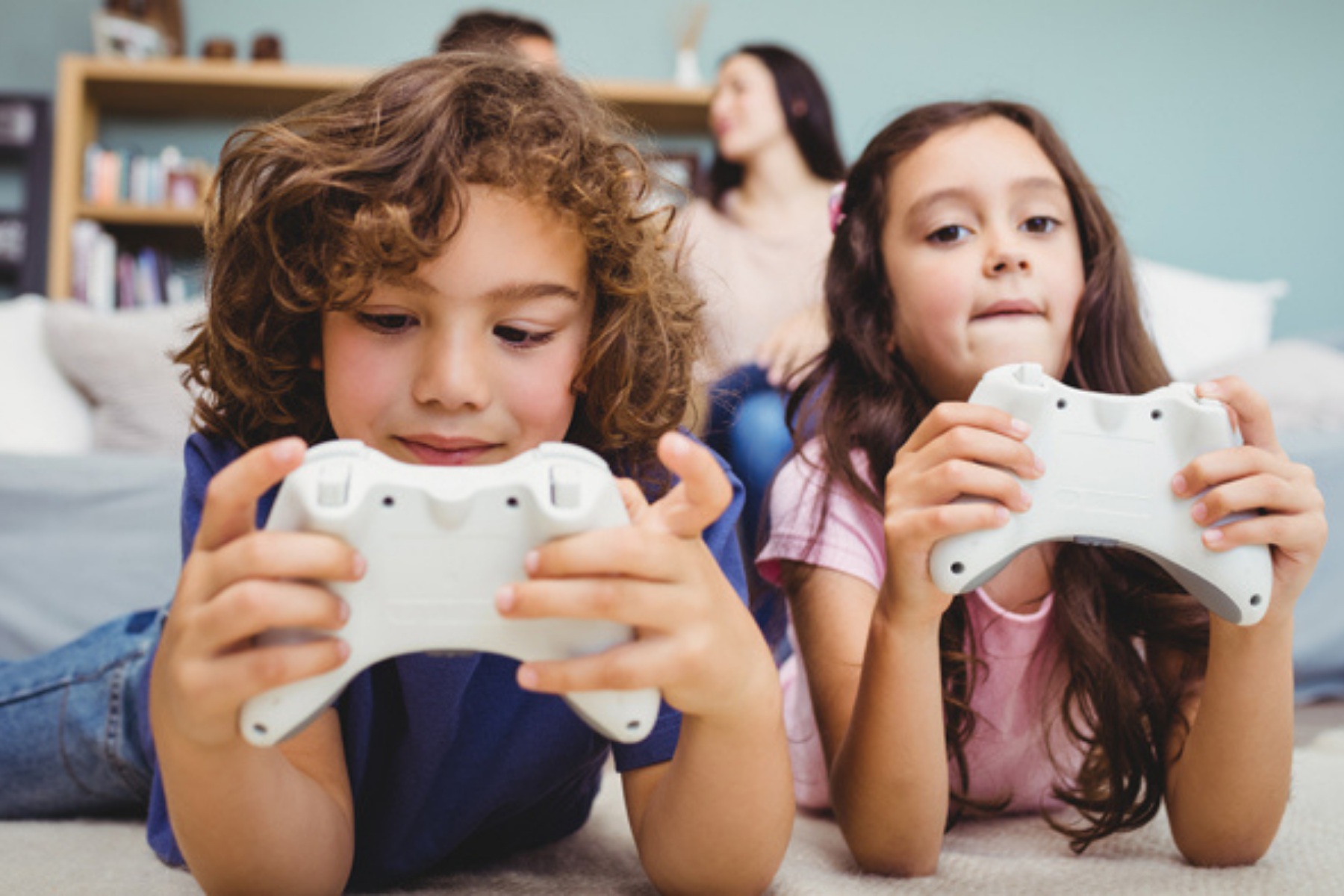 Zwei Kinder sitzen mit Spielkonsolen vor dem Bildschirm