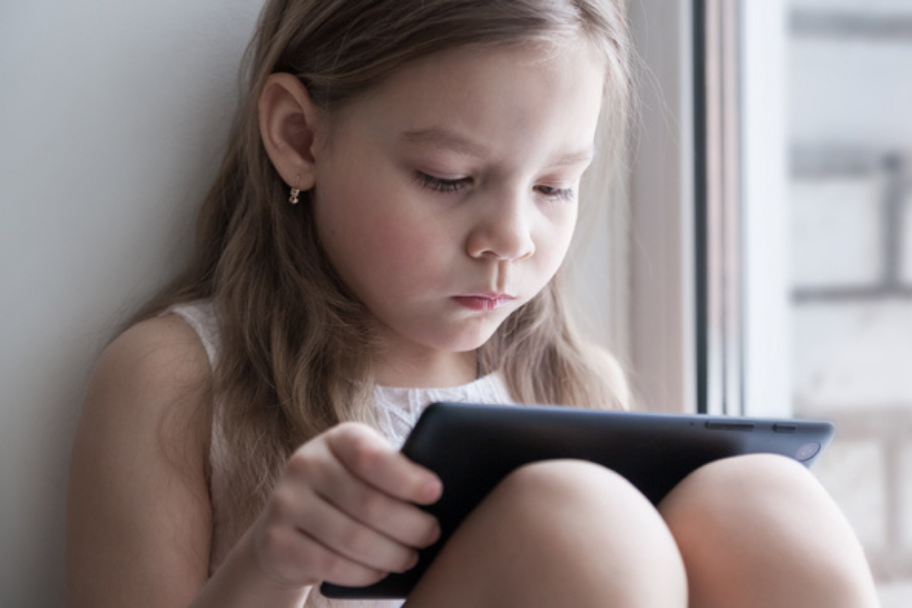 Kind sitzt auf dem Boden und und schaut in ein Tablet