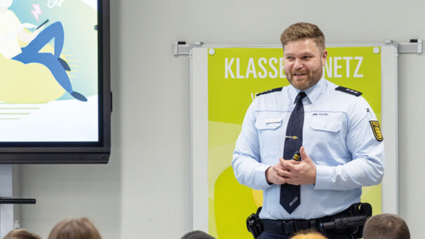 Ein Polizist in Uniform präsentiert in einer Schule an einem Bildschirm