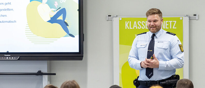 Ein Polizist in Uniform präsentiert in einer Schule an einem Bildschirm