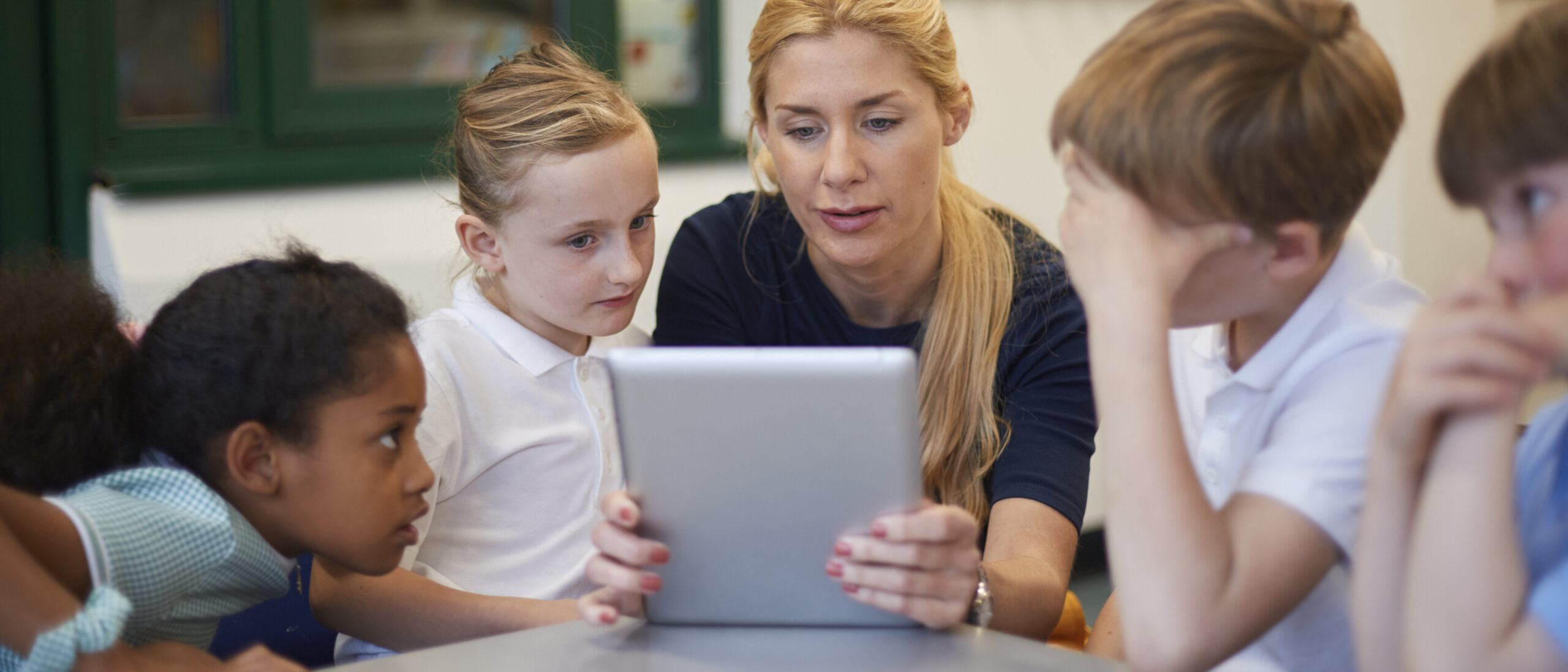 Der Lehrer zeigt den Schülern Inhalte auf einem Tablet in einem hell beleuchteten Klassenzimmer.